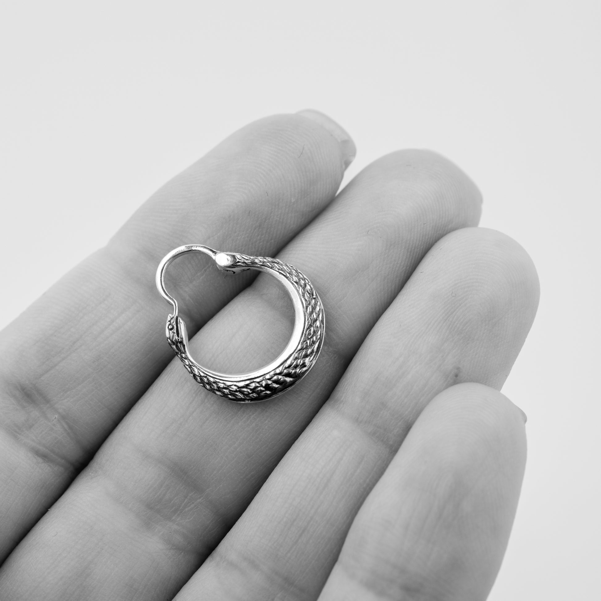 Silver hoop earring on a hand against a plain background