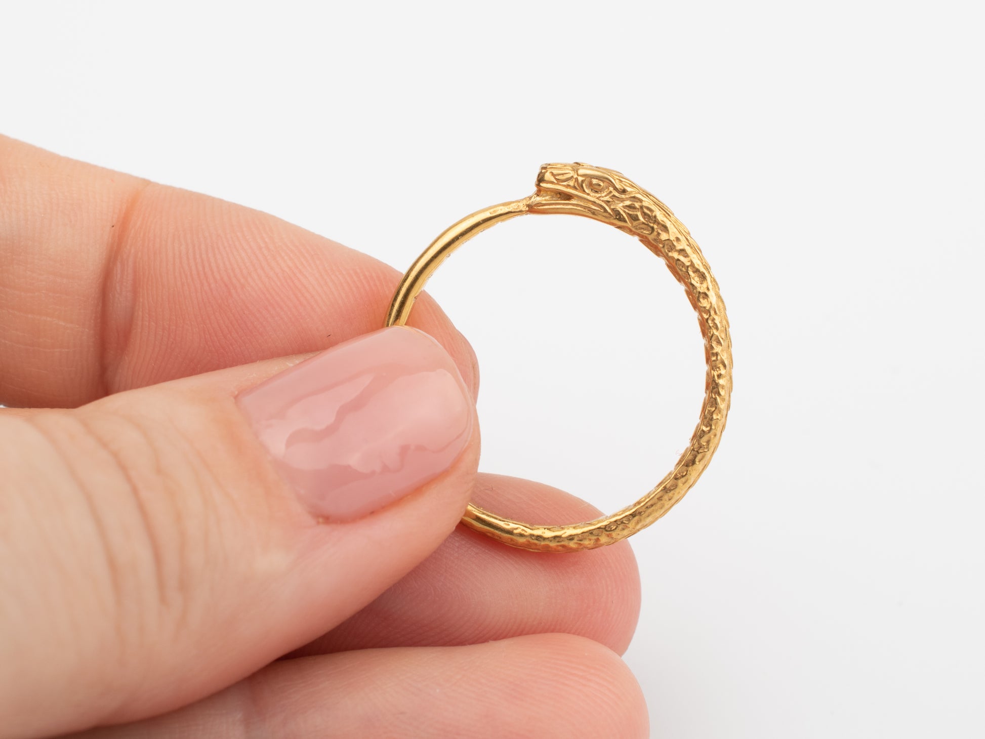 Gold ring with intricate design held by a hand for scale